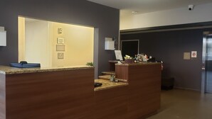 A reception desk with a computer monitor, a blue bowl, and a plant. There are signs on the wall and a door in the background. - Quality Inn & Suites Caldwell I-77 (Caldwell)