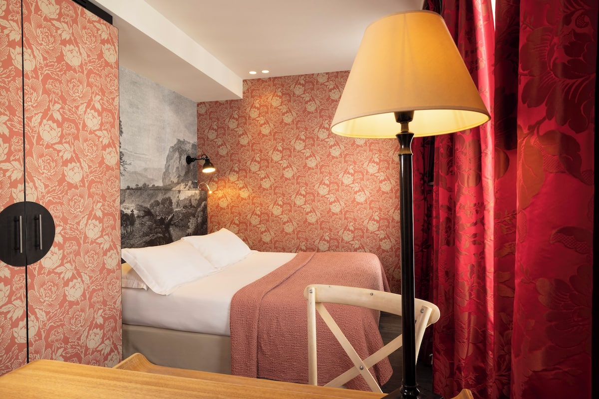 A bedroom with a bed, a nightstand, a lamp, and a wardrobe.