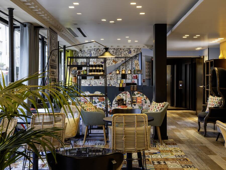 Un coin salon accueillant, avec des meubles en osier, un tapis à motifs et un mur décoré d’étagères remplies de bouteilles.