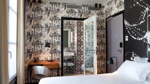 Ein Hotelzimmer mit Bett, Schreibtisch mit Lampe, einem Sessel und einem durchgegangenen Tür sichtbar erkennbaren Badezimmer.