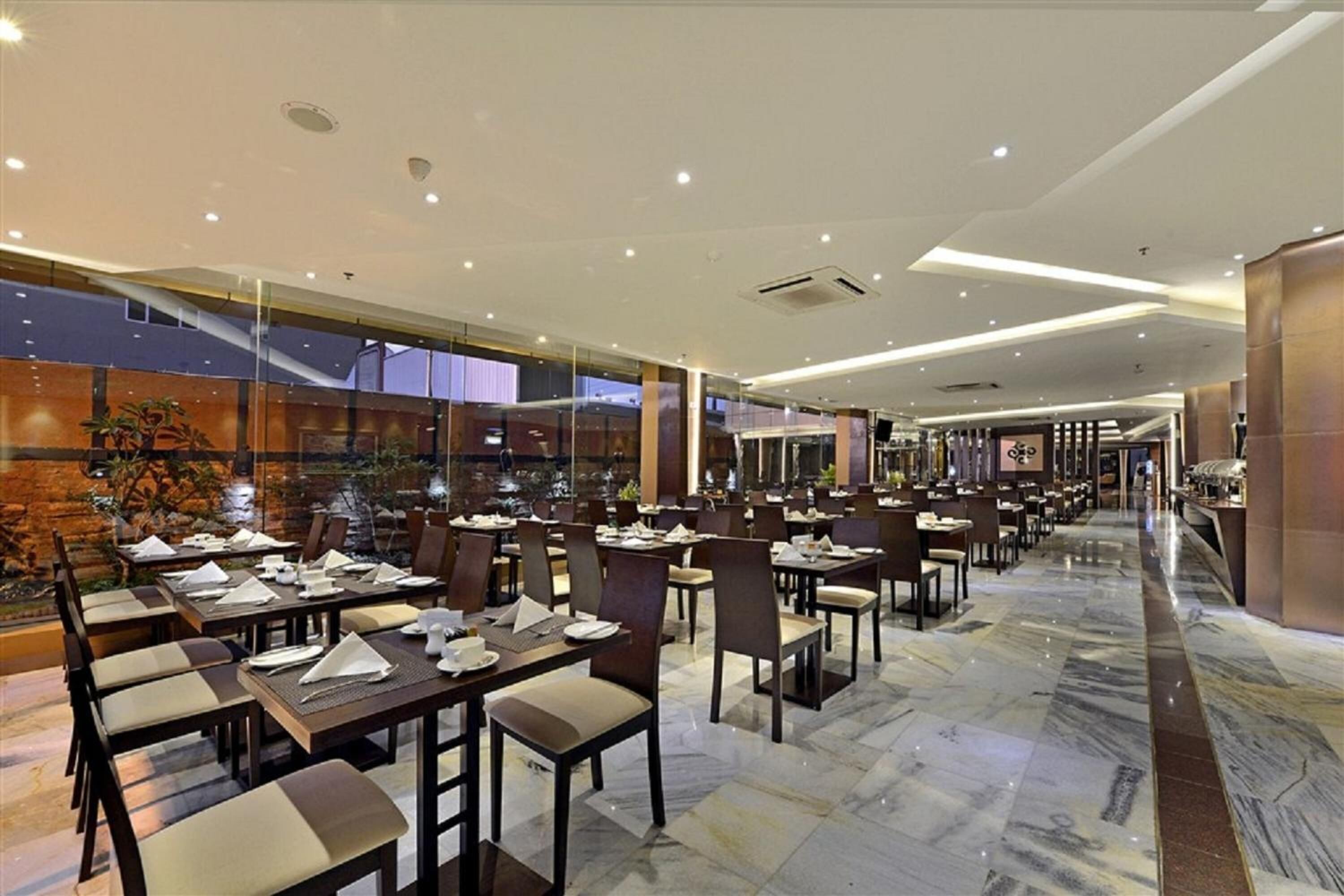 Un restaurant spacieux, doté de nombreuses tables et chaises, d’un sol en marbre et offrant une vue sur l’extérieur grâce à de grandes fenêtres.