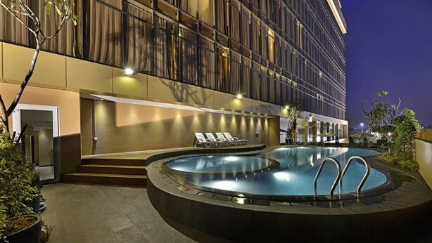 Een modern hotel met een rond zwembad, ligbedden en een goed verlichte ingang.