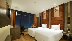 Hotelkamer met twee bedden, een bureau, een stoel, een televisie en een groot raam met gordijnen.