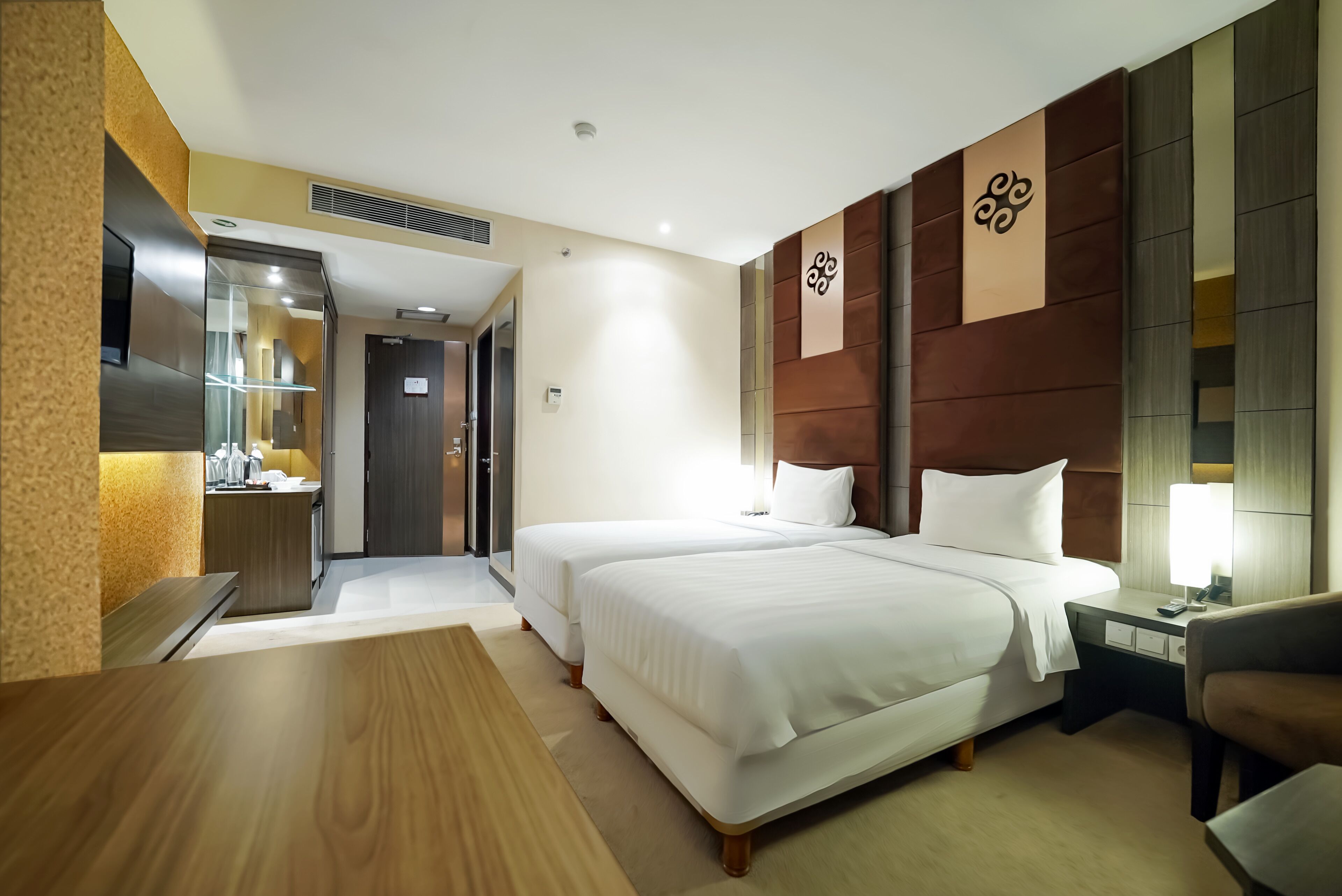 Une chambre d’hôtel avec deux lits, un bureau en bois, une chaise, une table de chevet avec une lampe et une œuvre d’art accrochée au mur.