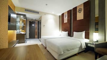 Une chambre d’hôtel avec deux lits, un bureau en bois, une chaise, une table de chevet avec une lampe et une œuvre d’art accrochée au mur.