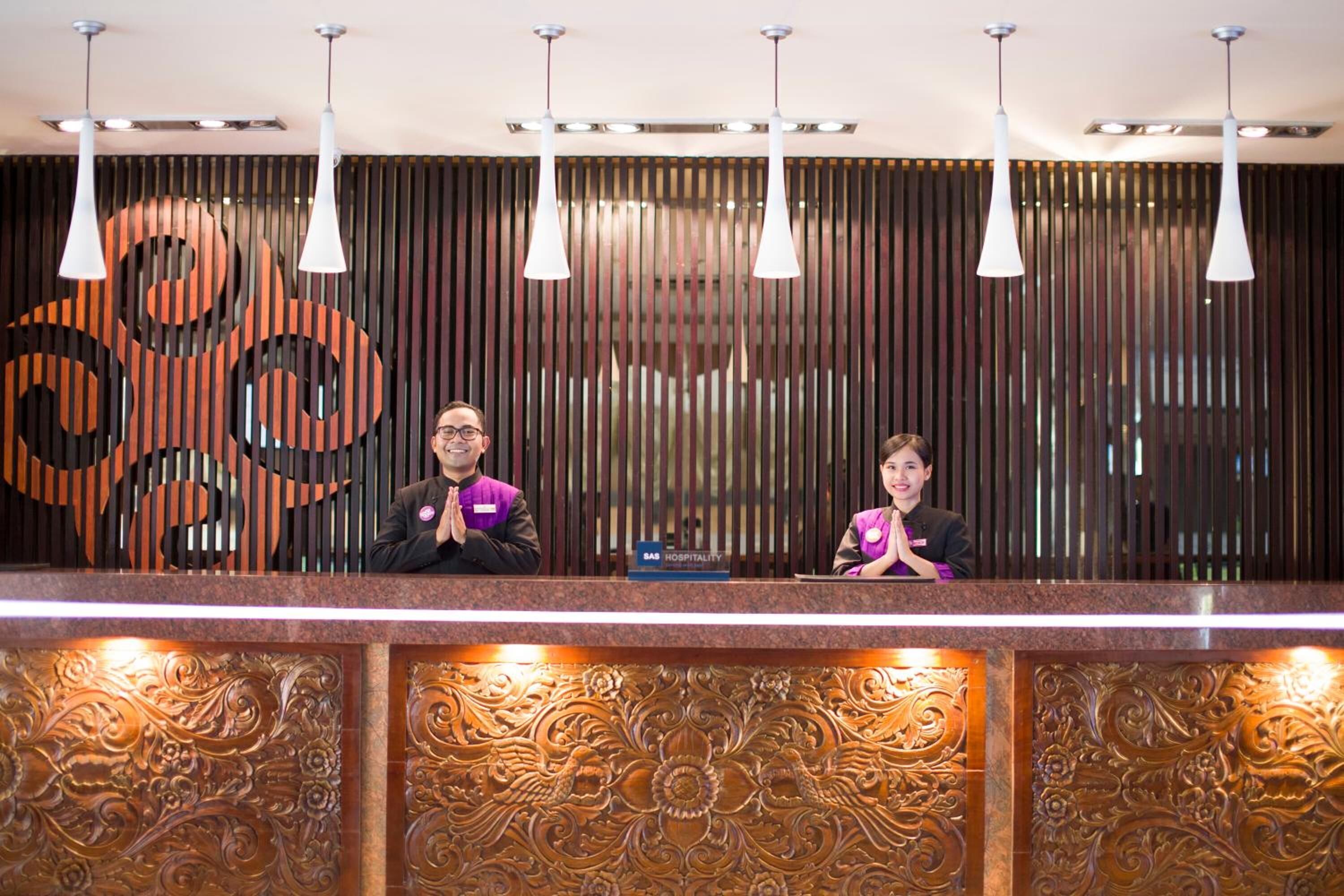 Una recepción con dos empleados, una pared decorativa con listones verticales e iluminación colgante.