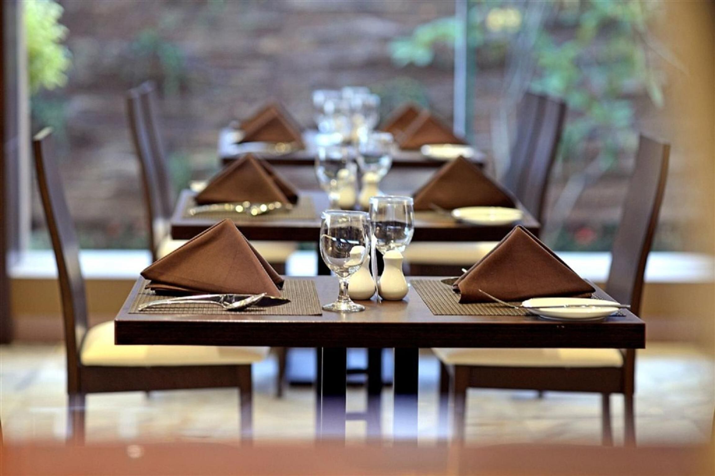 A dining table set with brown napkins, silverware, and clear glasses, with chairs around it.