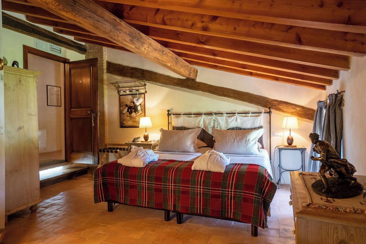 Une chambre confortable avec un plafond en bois, un lit recouvert d  ’une couverture à carreaux, deux tables de chevet avec des lampes et une statue posée sur une petite table d’appoint.