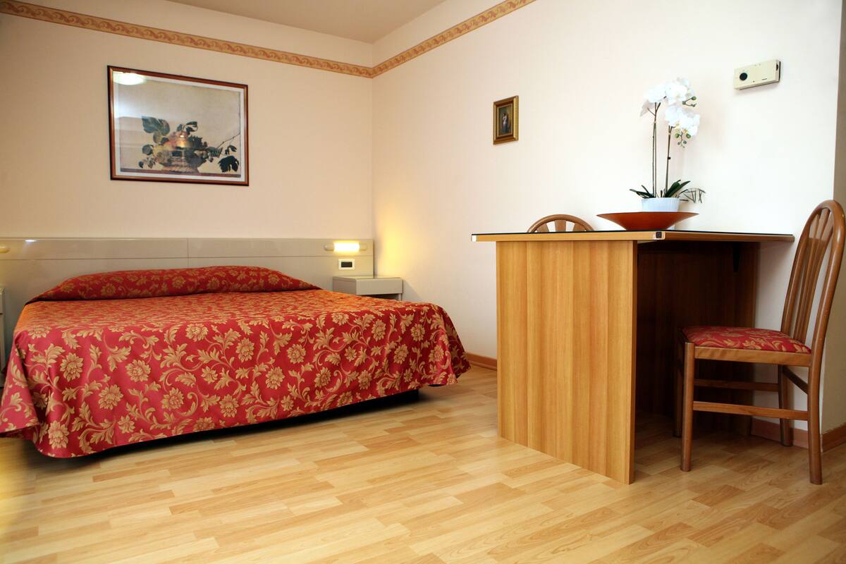 Une chambre d’hôtel avec un lit, un bureau, une chaise et une plante en pot.