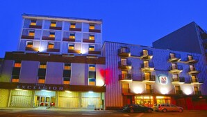 Ein Hotel mit mehreren Etagen, einem markanten Eingang und einem Parkplatz.