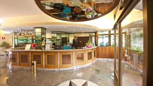 Eine Hotelhalle mit einer gebogenen Rezeption, einem großen Spiegel und einer modernen Chandelier.