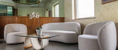 A modern room with a curved white sofa, a glass coffee table, and a potted plant.