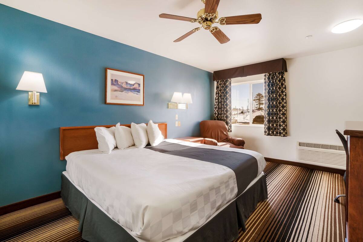 Une chambre d’hôtel avec un grand lit, un ventilateur de plafond, un bureau et une fenêtre avec des rideaux.