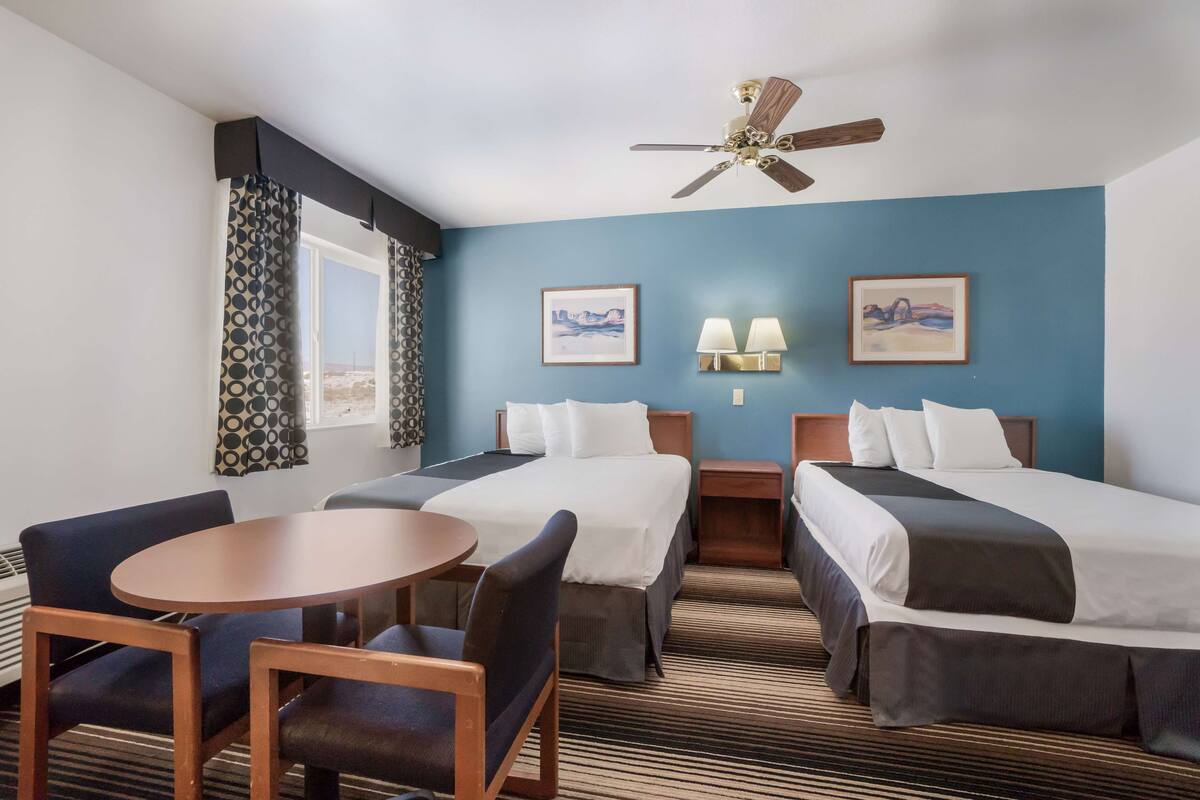 Une chambre d’hôtel avec deux lits, une table ronde et deux chaises. Il y a deux lampes fixées au mur et un ventilateur de plafond.