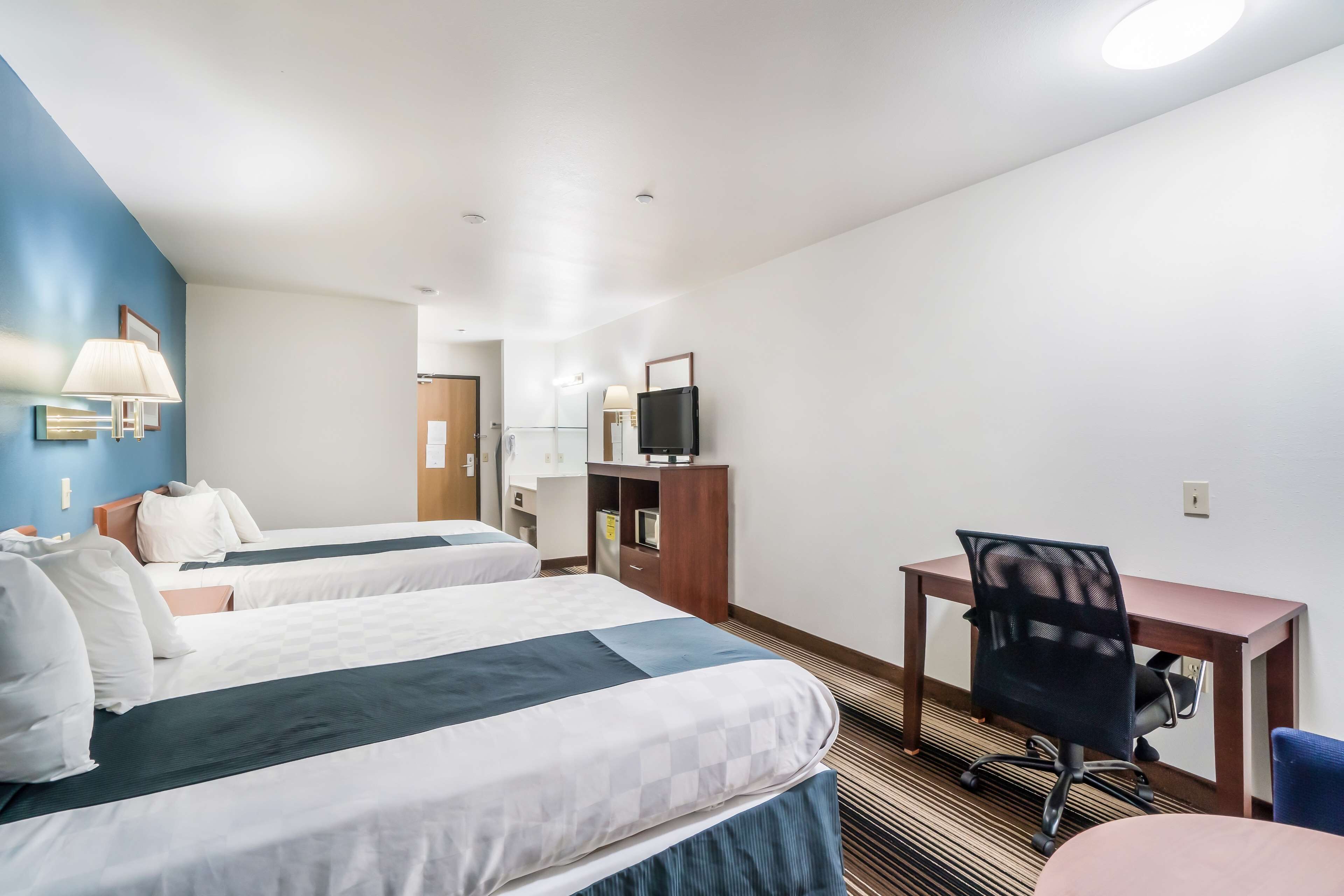 A hotel room with two beds, a desk, a chair, a TV, and a bathroom visible in the background.
