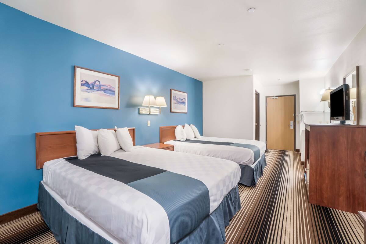 Une chambre d’hôtel avec deux lits, un bureau, une télévision et des œuvres d’art accrochées aux murs.