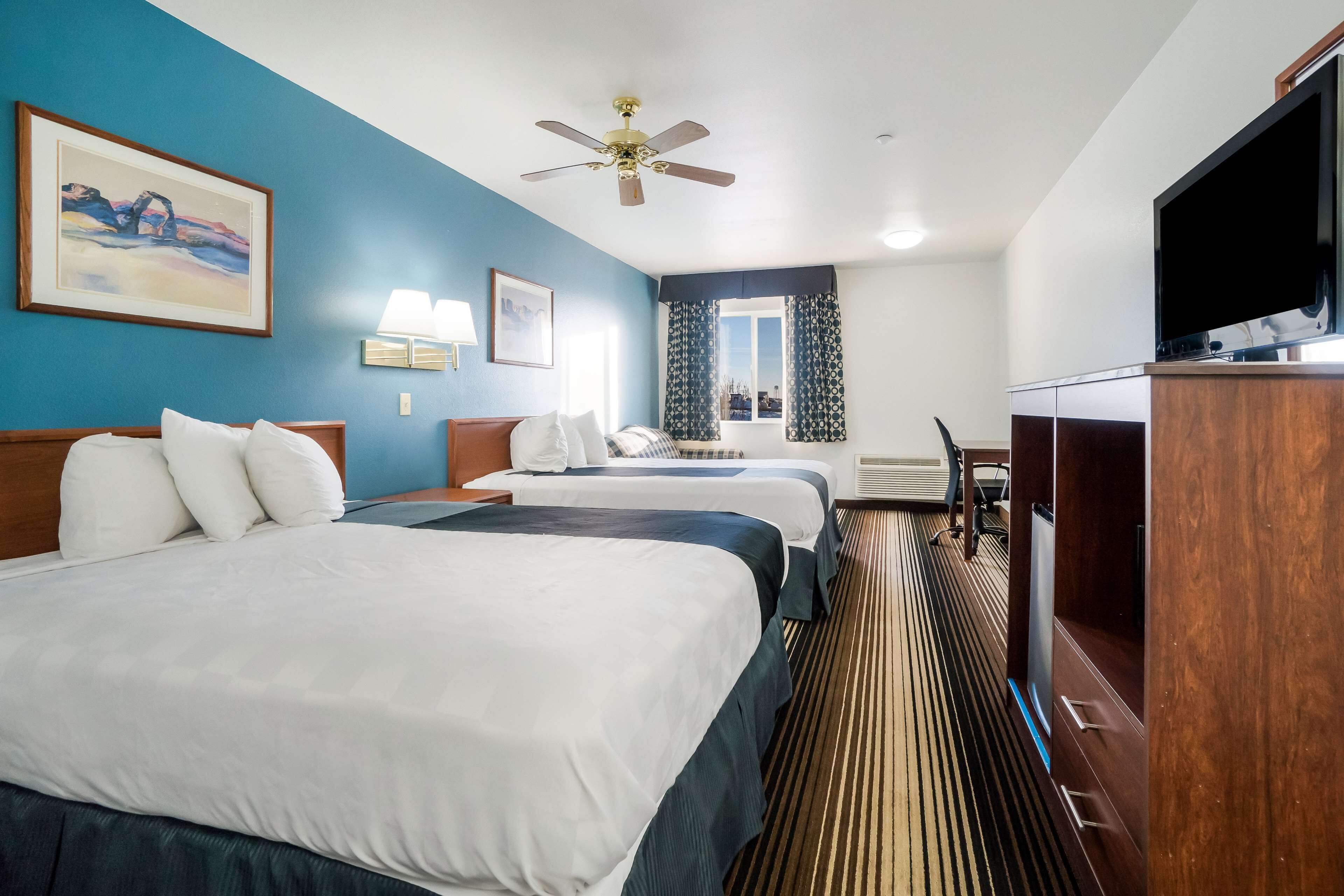 A hotel room with two beds, a television, a ceiling fan, and a window with curtains.