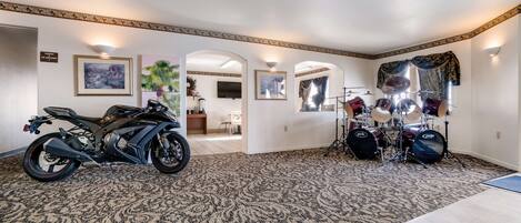 A spacious room with a patterned carpet, a motorcycle, a drum set, and framed artwork on the walls.