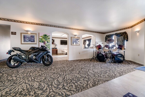 A spacious room with a patterned carpet, a motorcycle, a drum set, and framed artwork on the walls.