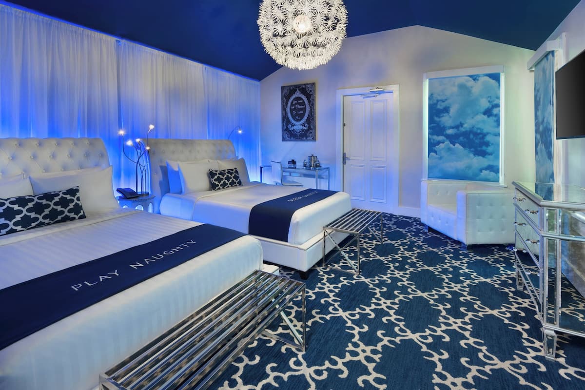 A hotel room with two beds, a chandelier, a large window with a view, and a patterned carpet.