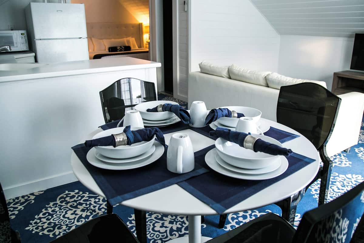 A dining area with a round table set for four, white plates, bowls, and a teapot, with blue napkins and placemats.