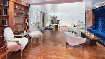 Une pièce spacieuse dotée d’un plancher en bois, d’un canapé bleu recouvert de tissu, d’un fauteuil blanc et d’une bibliothèque remplie de livres et d’objets décoratifs.