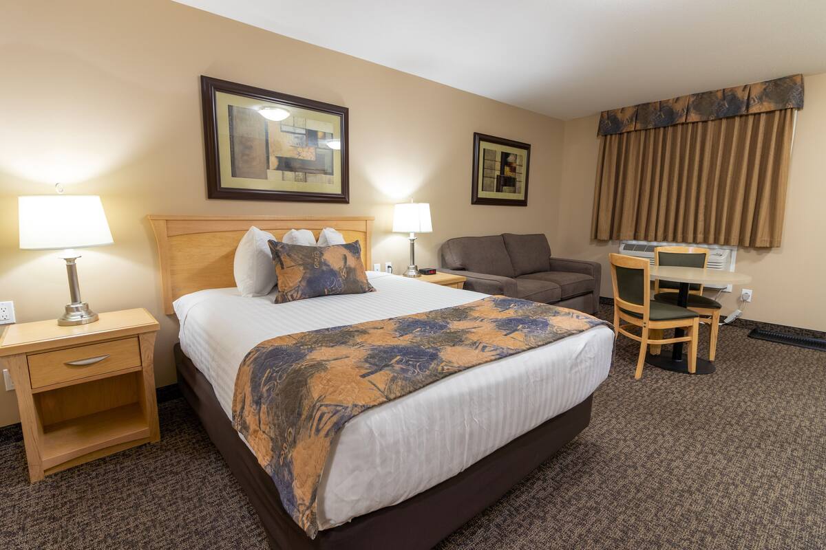 A hotel room with a large bed, two bedside tables with lamps, a desk with a chair, and two framed pictures on the wall.