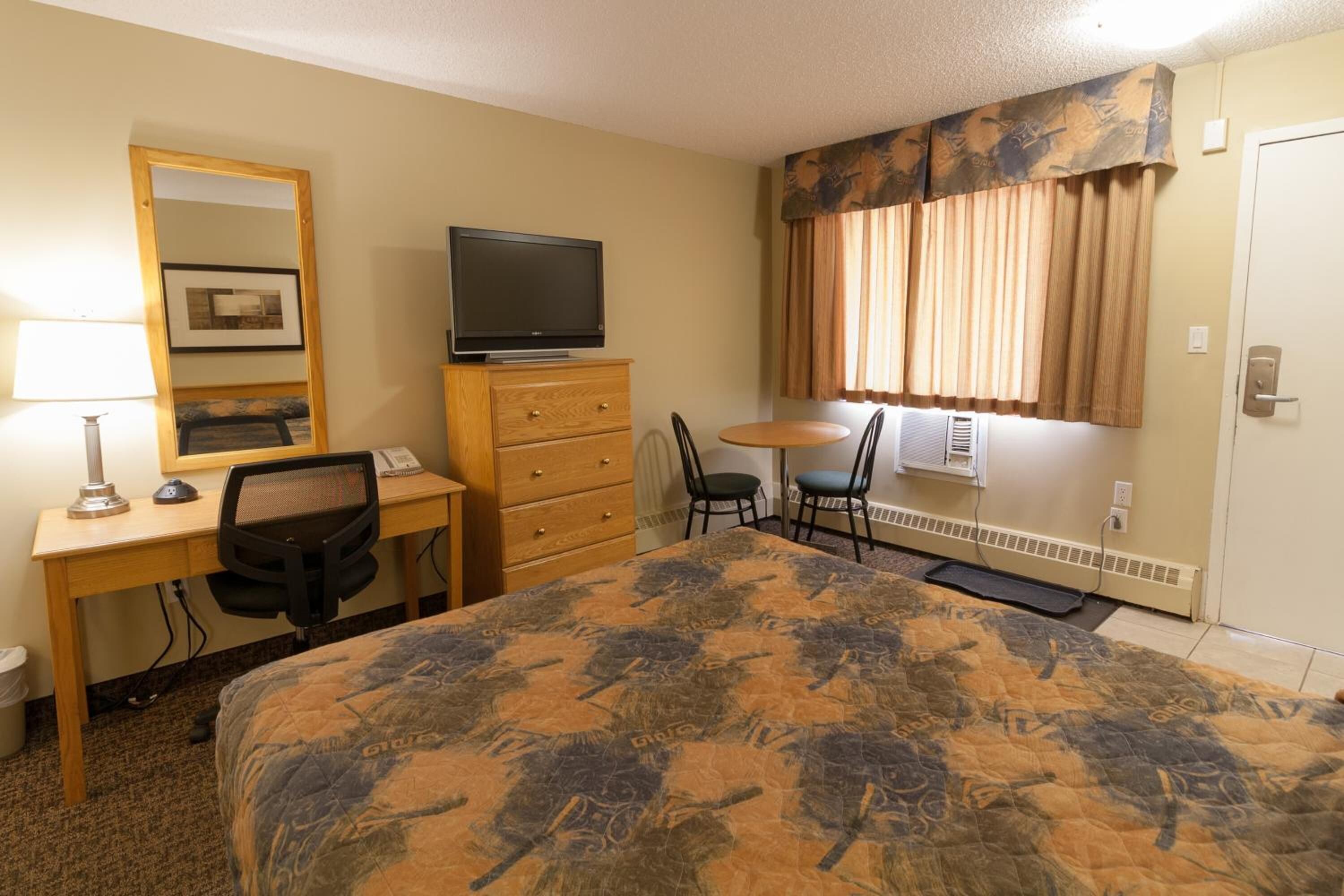 Una habitación de hotel con una cama, un escritorio con computadora, televisor, una silla y una mesita.