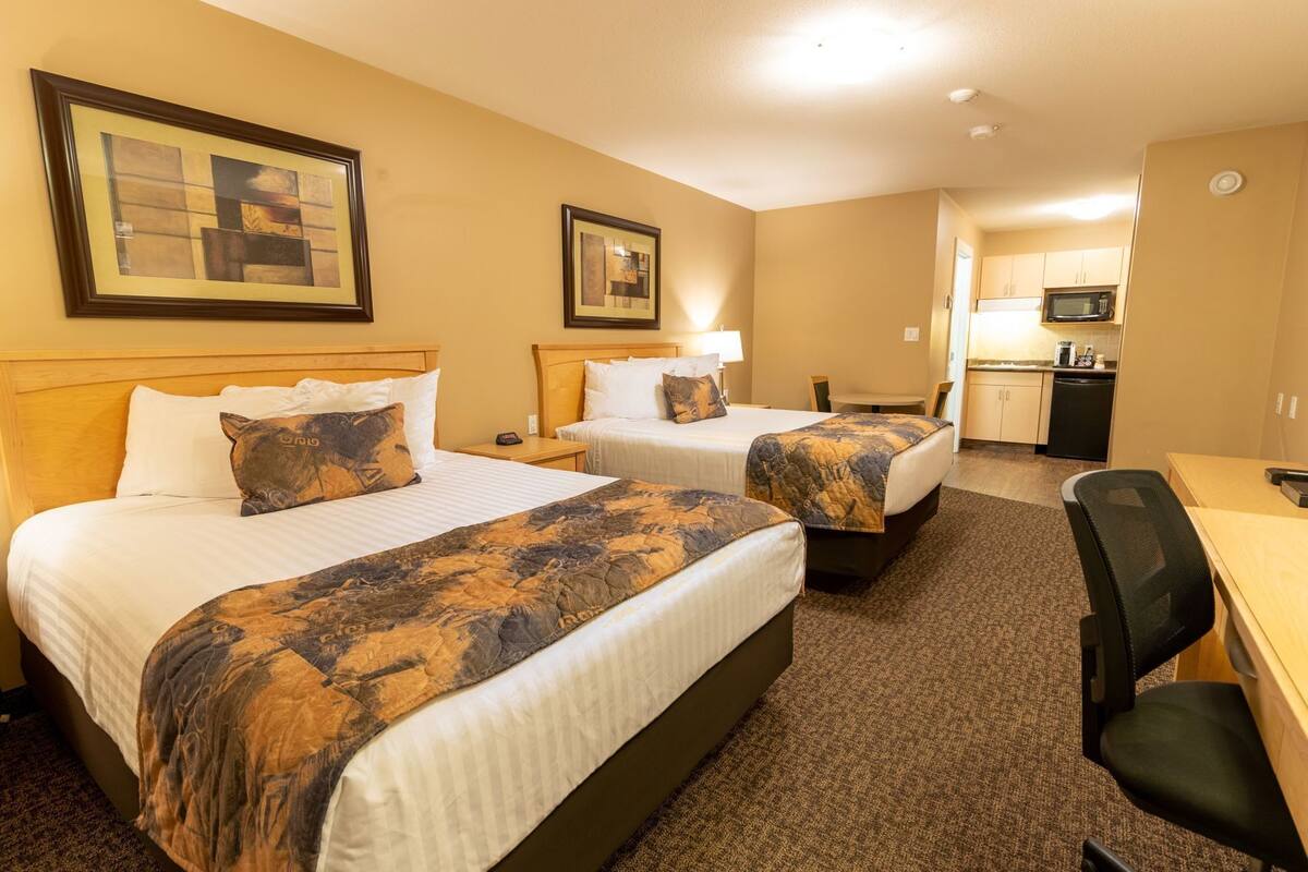 A hotel room with two beds, a desk, a chair, a microwave, and a small kitchenette.