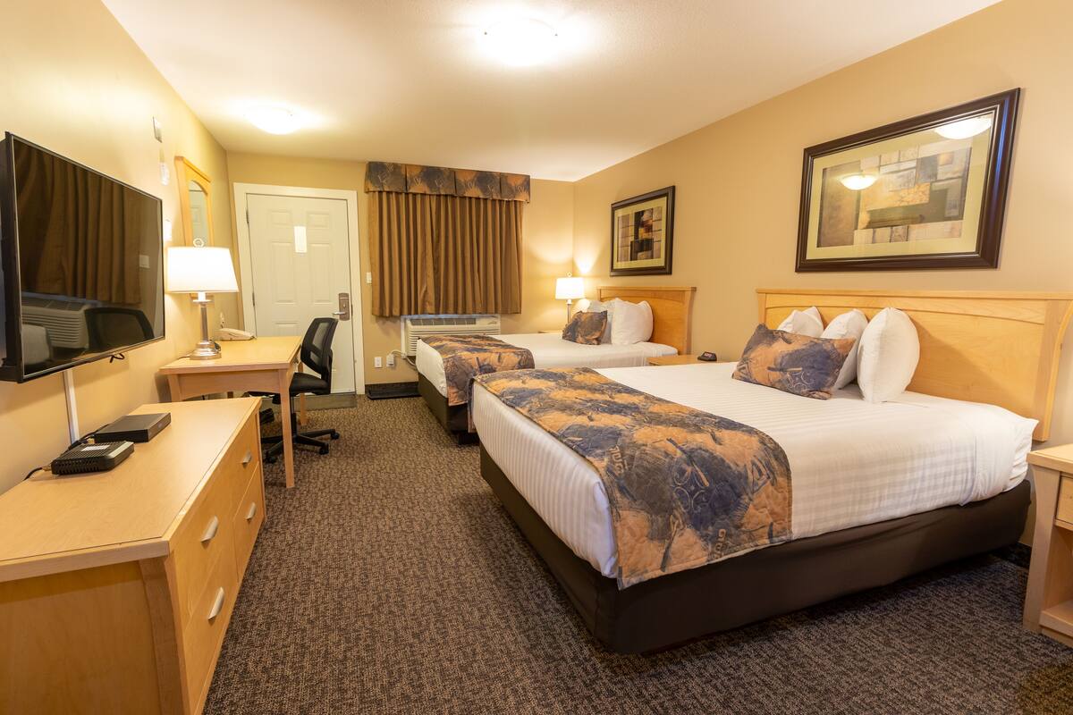 A hotel room with two beds, a desk, a chair, a TV, and a framed picture on the wall.