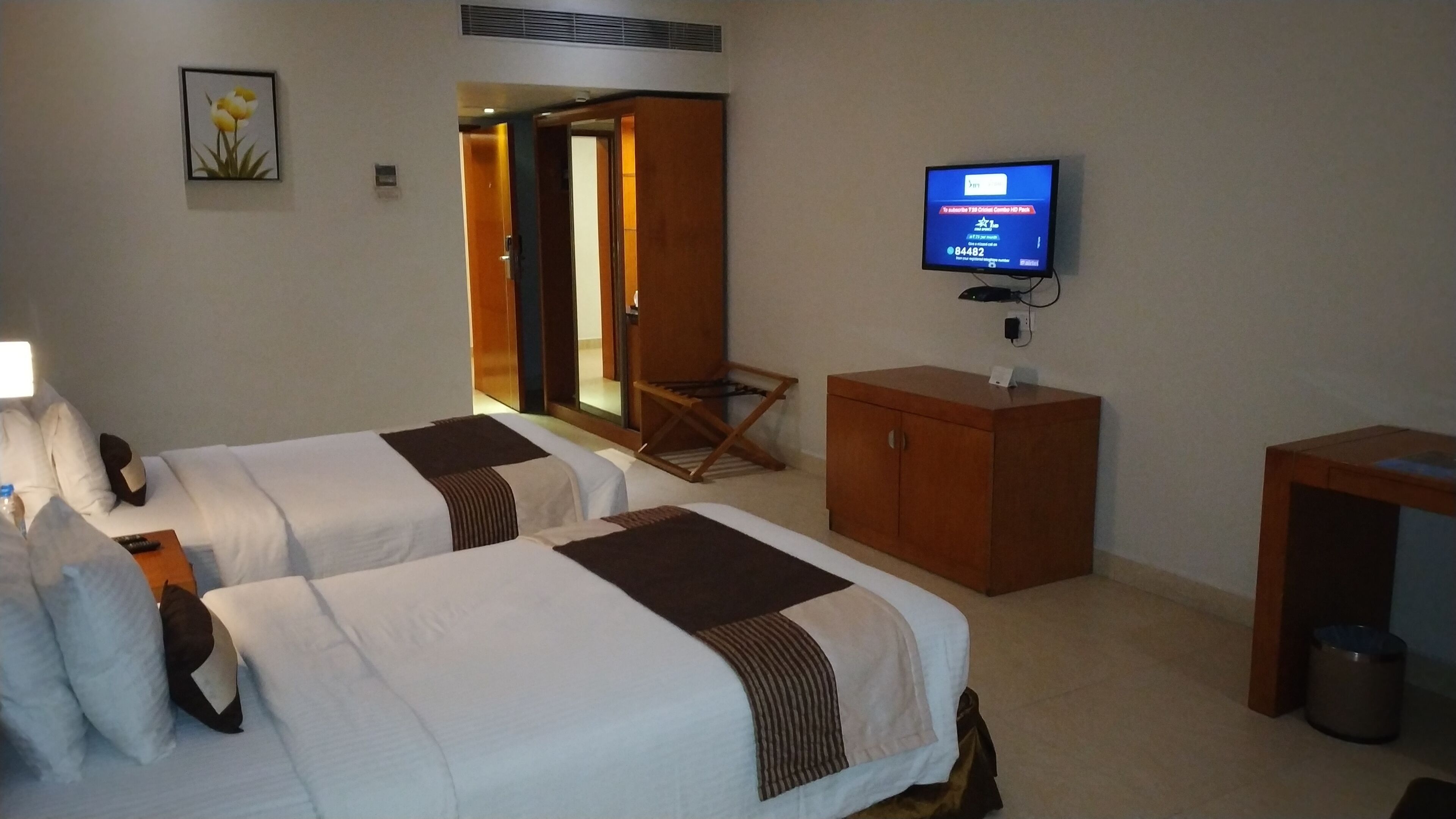 A hotel room with two beds, a TV, a wooden cabinet, and a small table.