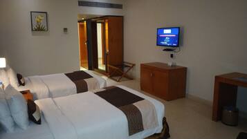 A hotel room with two beds, a TV, a wooden cabinet, and a small table.