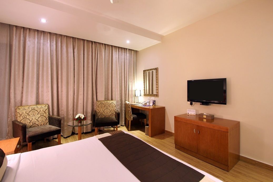 A hotel room with a bed, two armchairs, a desk, a television, and a cabinet.