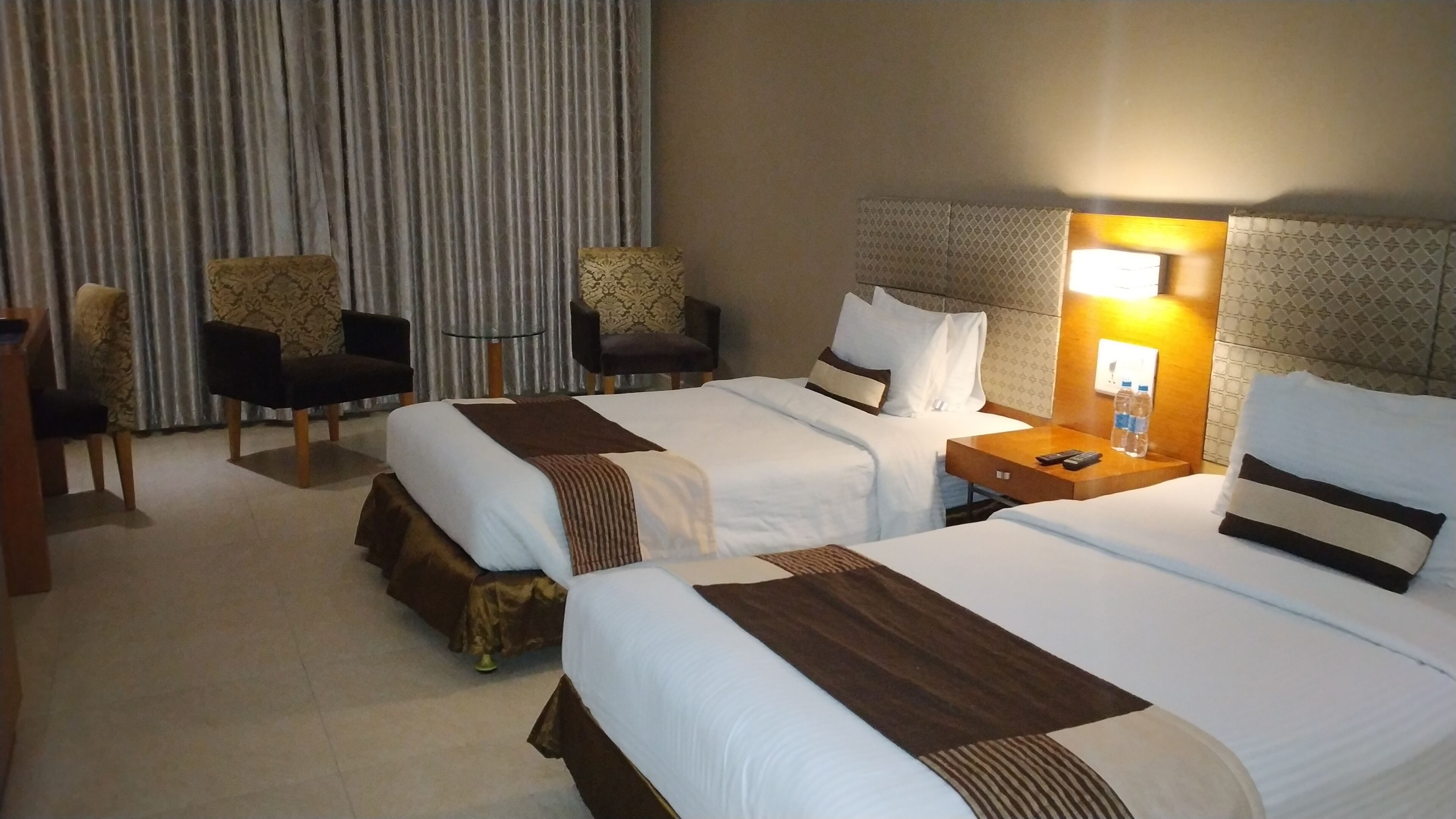 A hotel room with two beds, a desk, a chair, and a small table.