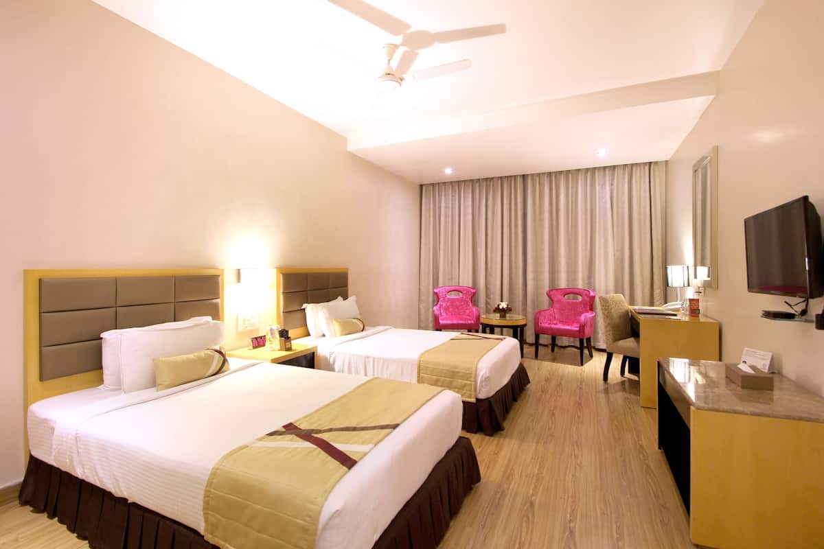 A hotel room with two beds, a desk, a chair, a television, and a ceiling fan.