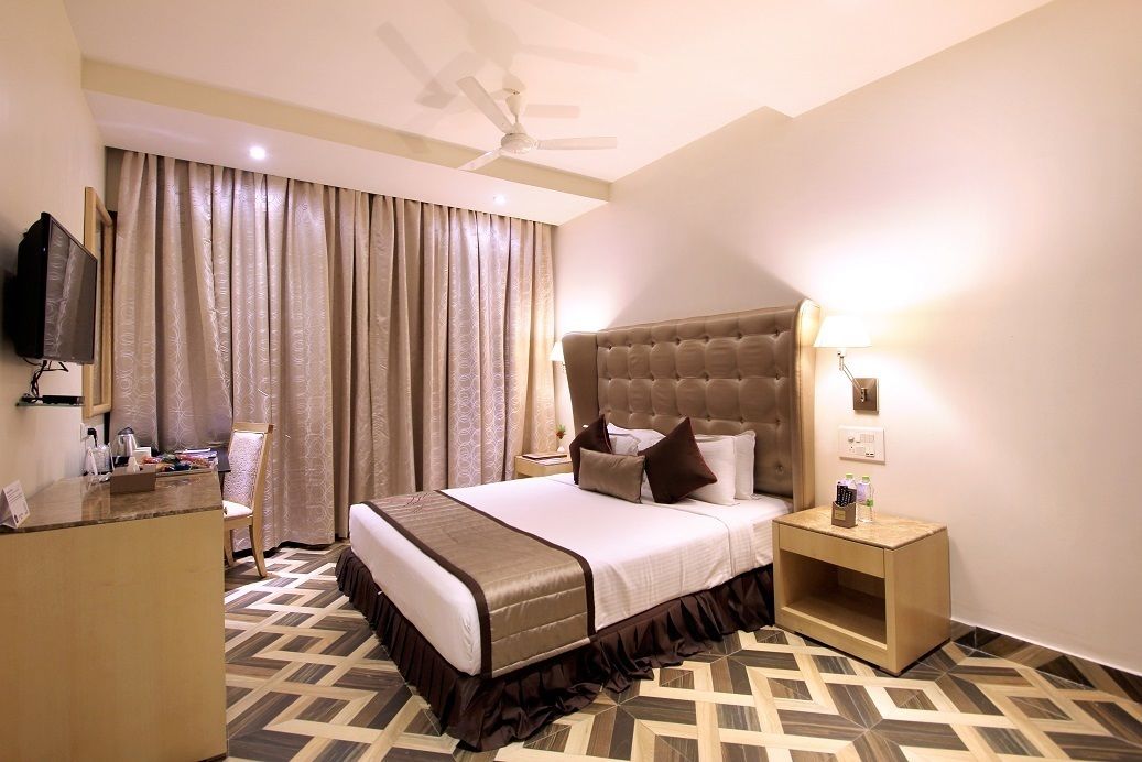 A hotel room with a large bed, a television on a stand, a desk, and a nightstand with a lamp.