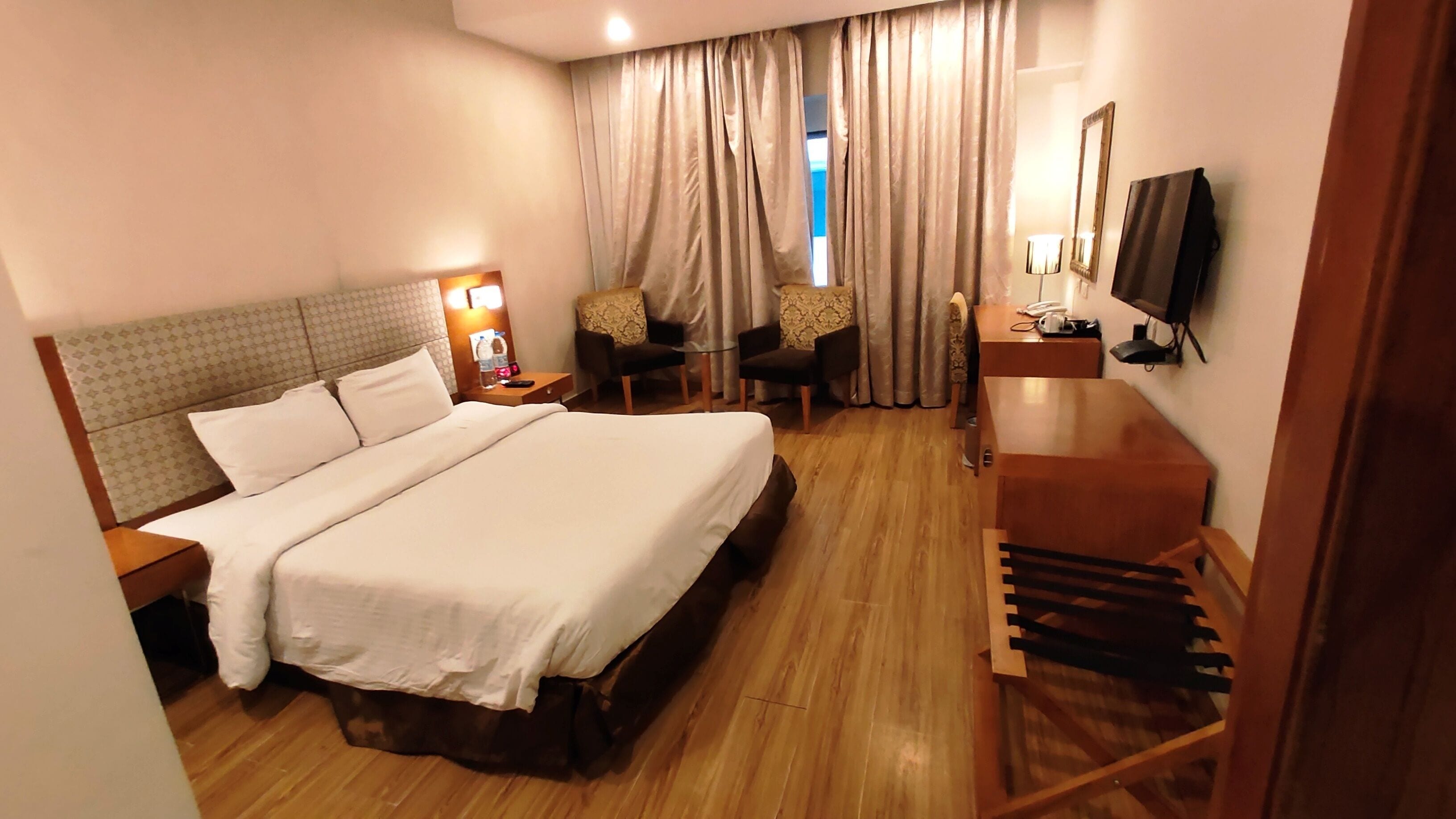 A hotel room with a large bed, a desk with a chair, a TV, and a window with curtains.