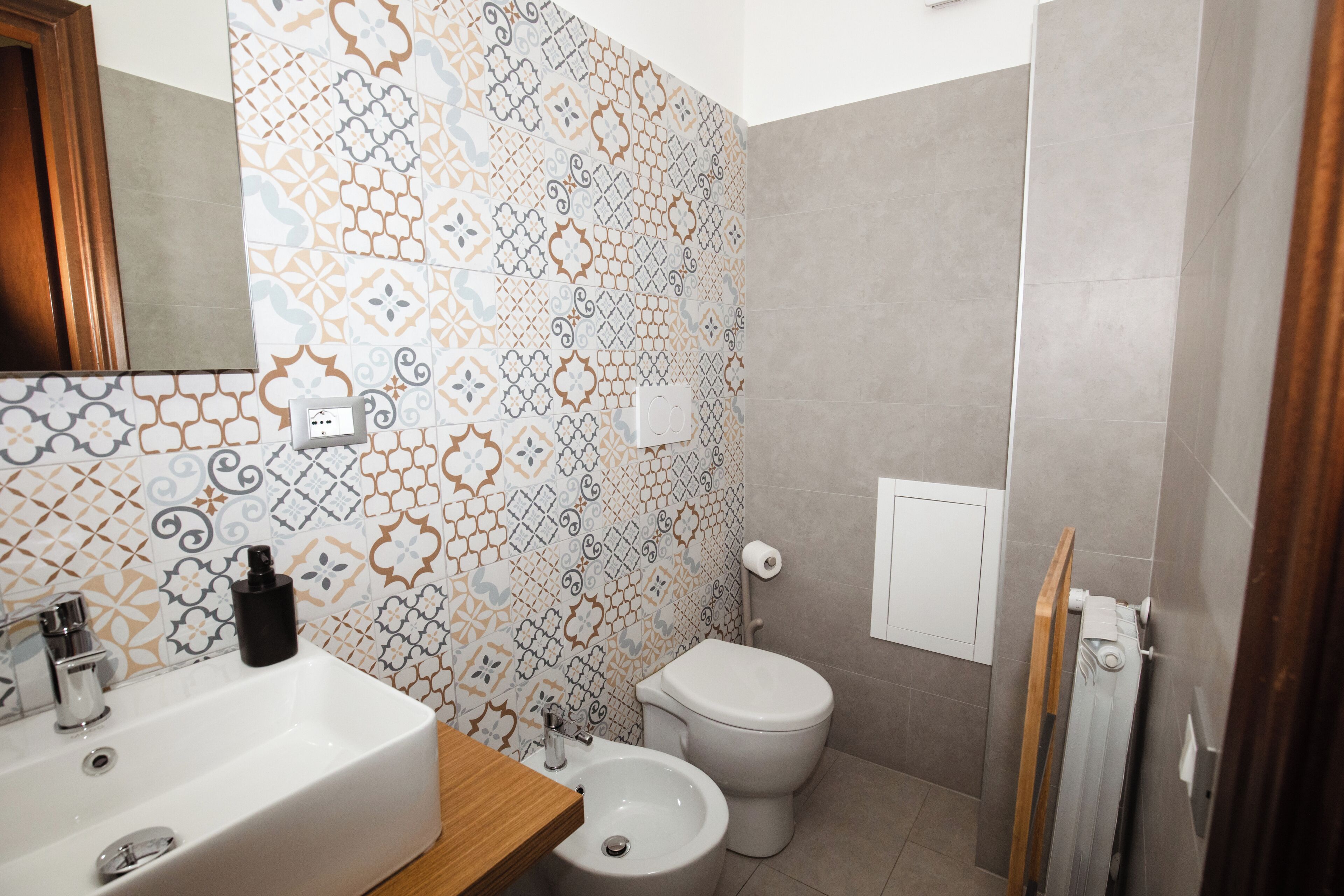 Un baño con lavamanos blanco, un bidé y un inodoro. Las paredes están decoradas con azulejos estampados.