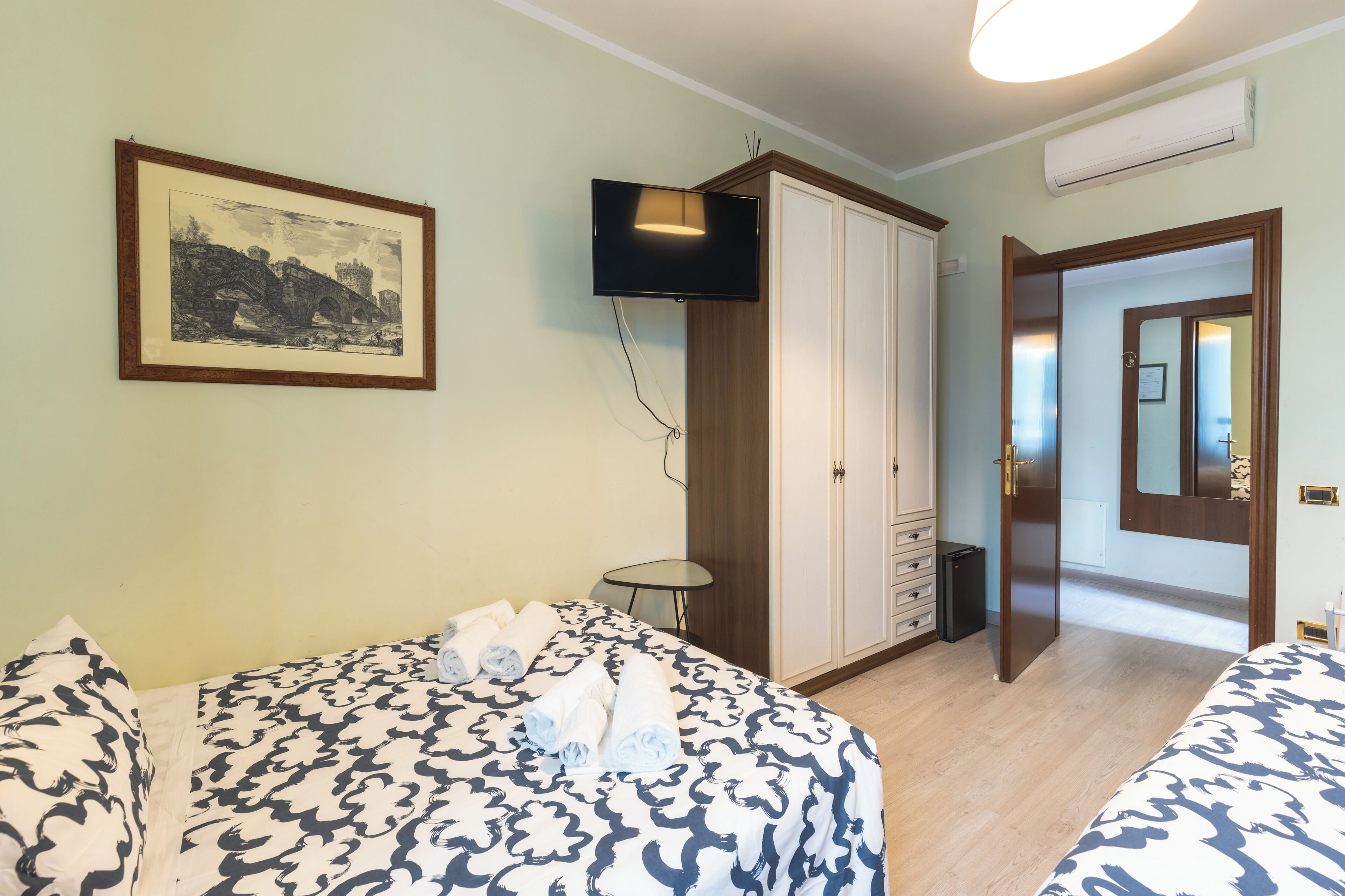 Habitación de hotel con cama, una mesita, un armario y televisión montada en la pared.