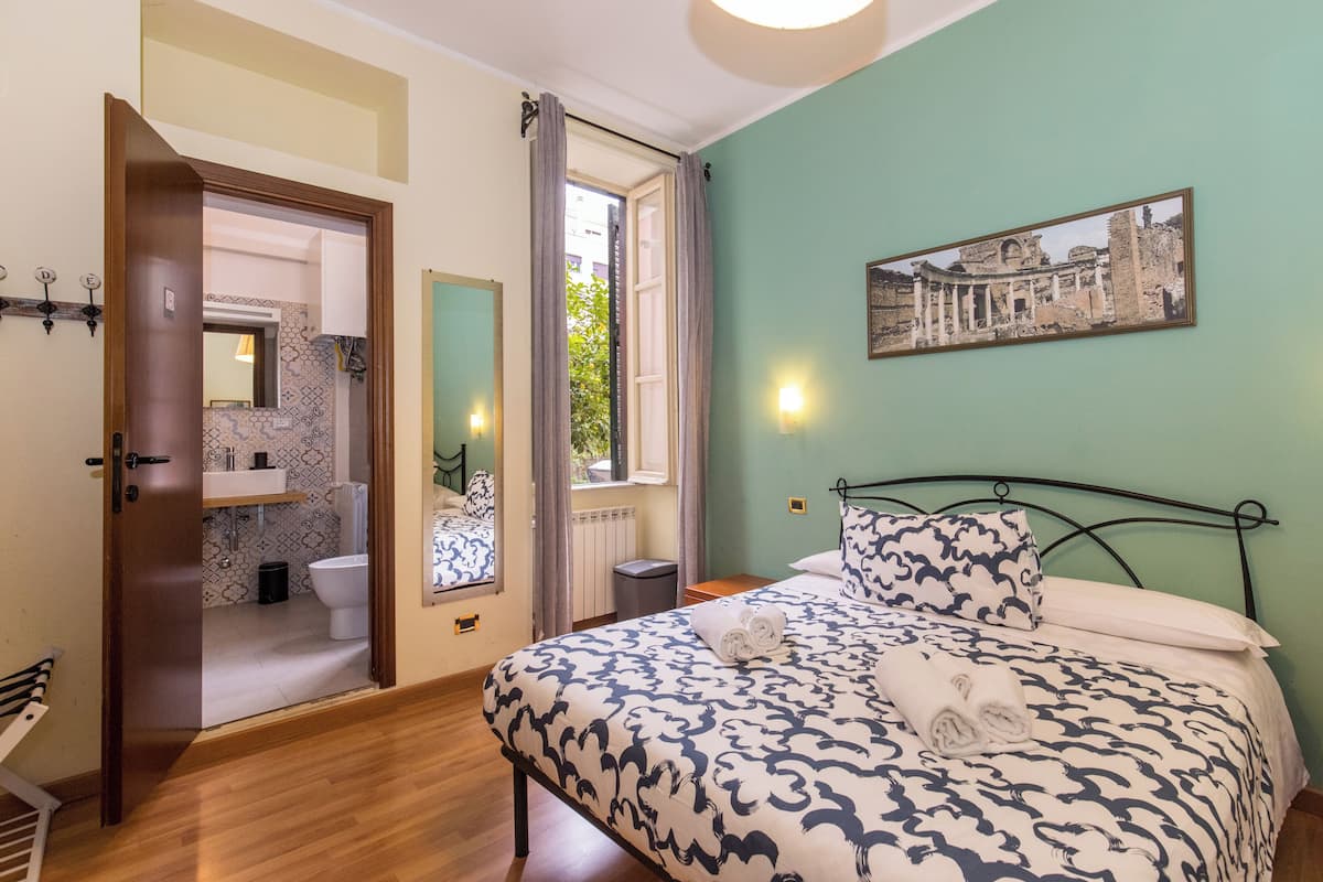 A bedroom with a patterned bedspread, a framed picture on the wall, and a view of the bathroom through an open door.