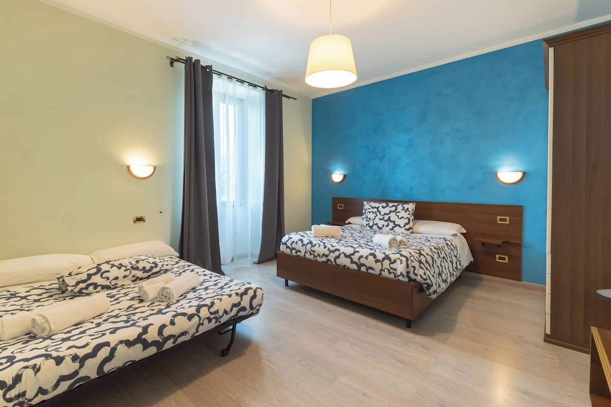 A hotel room with a bed, a sofa, and a window with curtains.