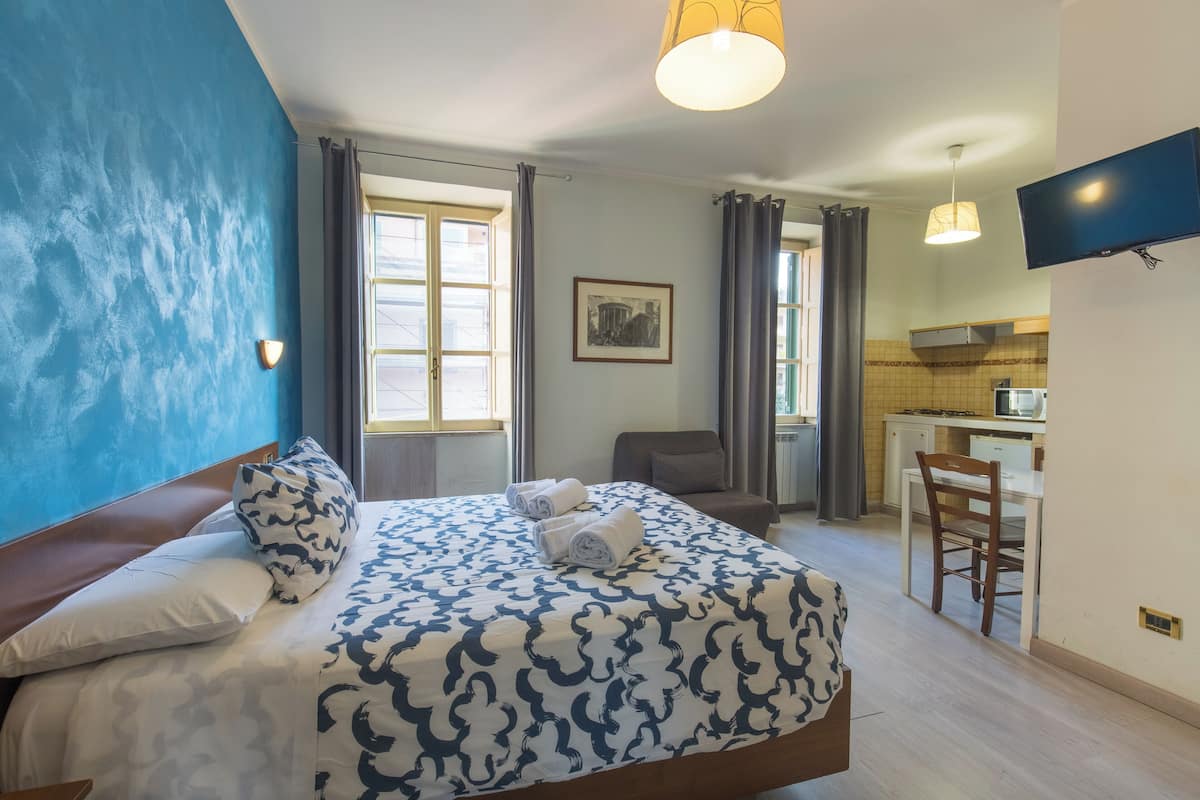 A hotel room with a bed, a desk, a chair, a television, and a window.
