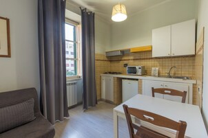 Cocina compacta con comedor, sofá y ventana con cortinas.
