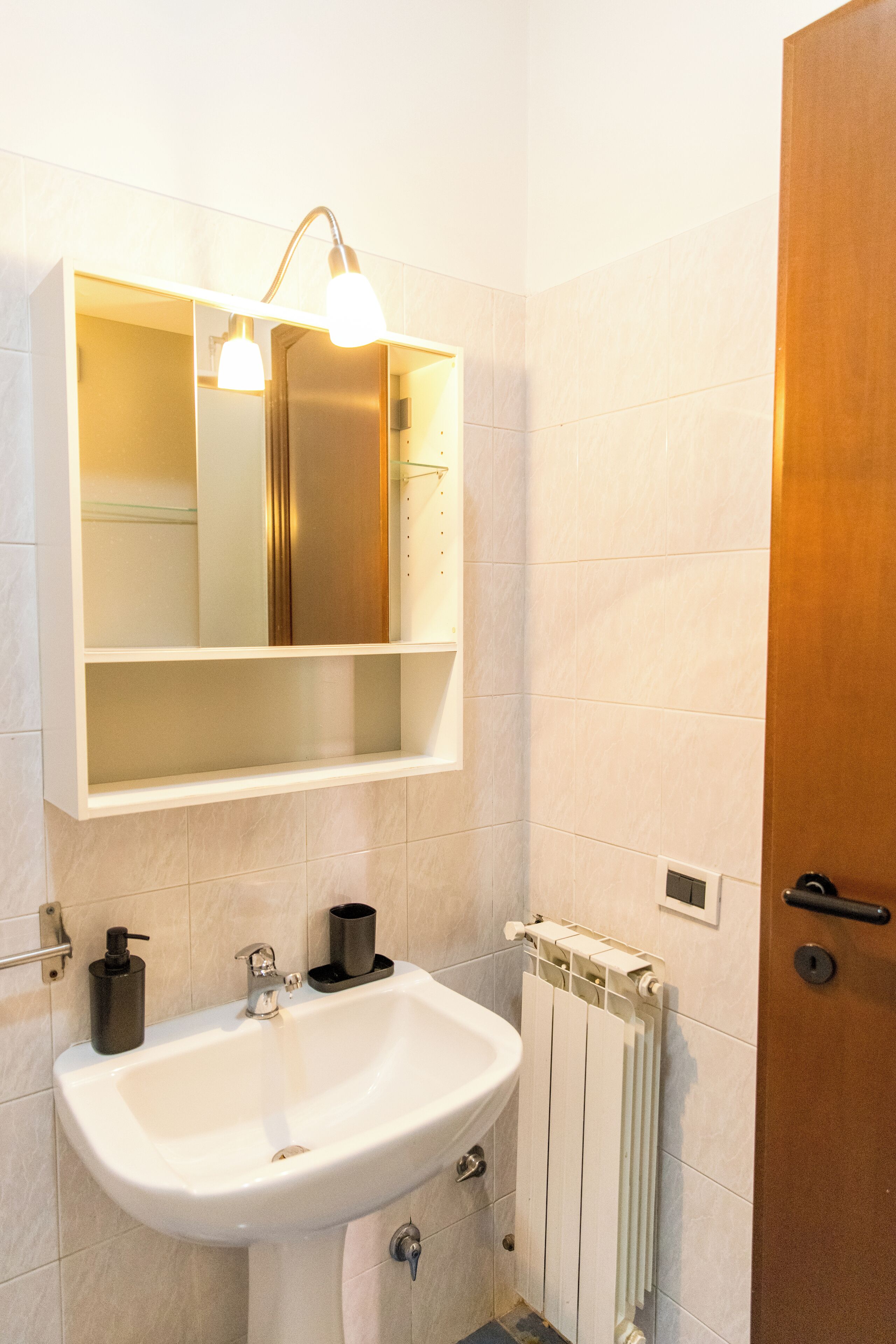 Un baño con un lavabo blanco, un espejo, una lámpara y un radiador.