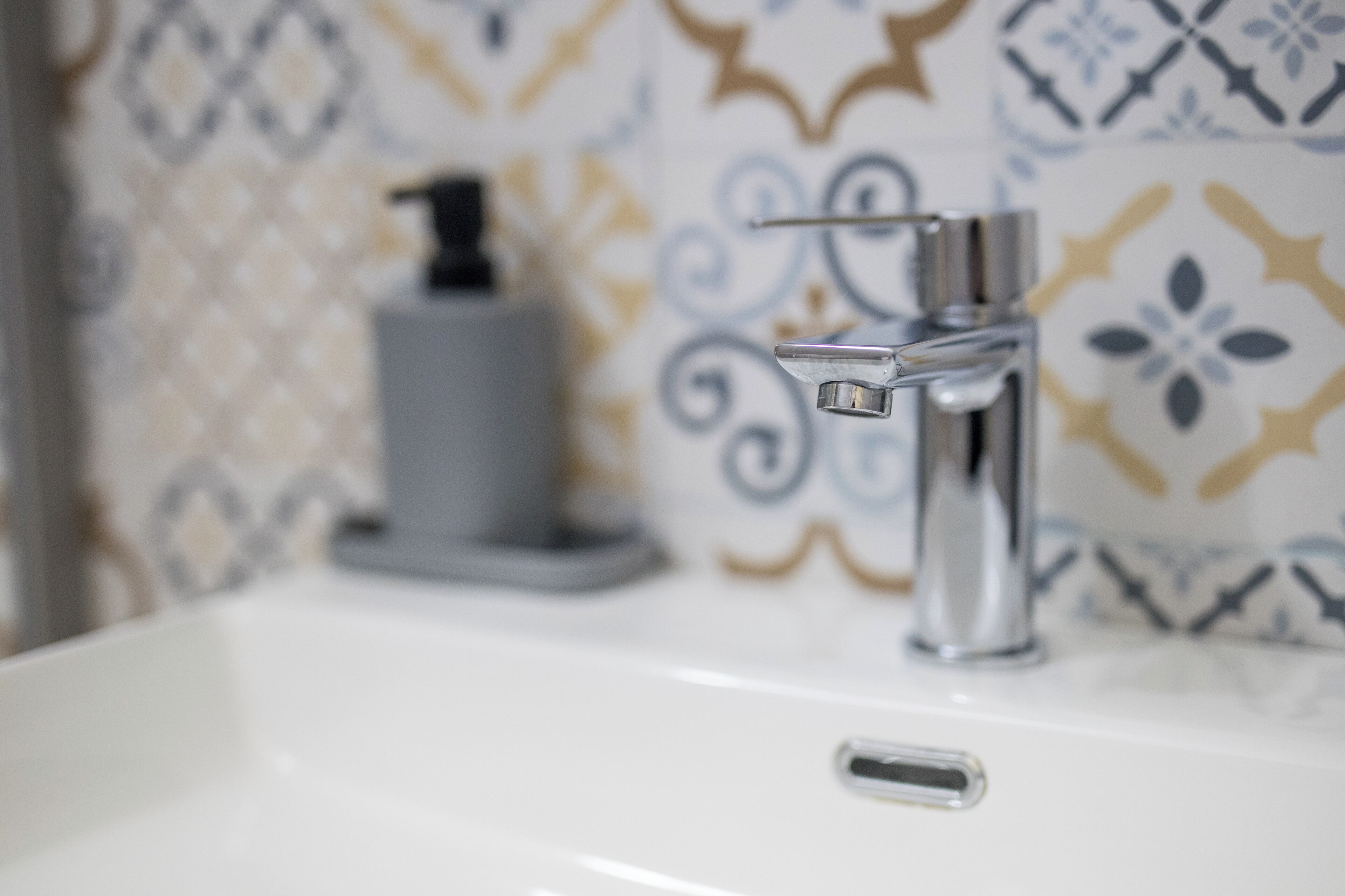 Un lavamanos de baño con una llave moderna y un dispensador de jabón.