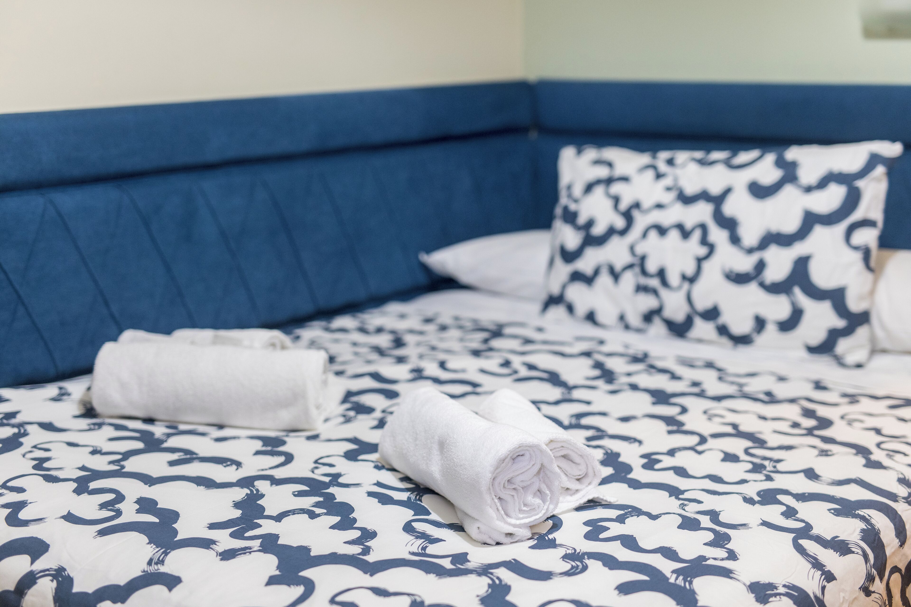 A bed with a blue headboard, white and blue patterned bedding, and rolled white towels.