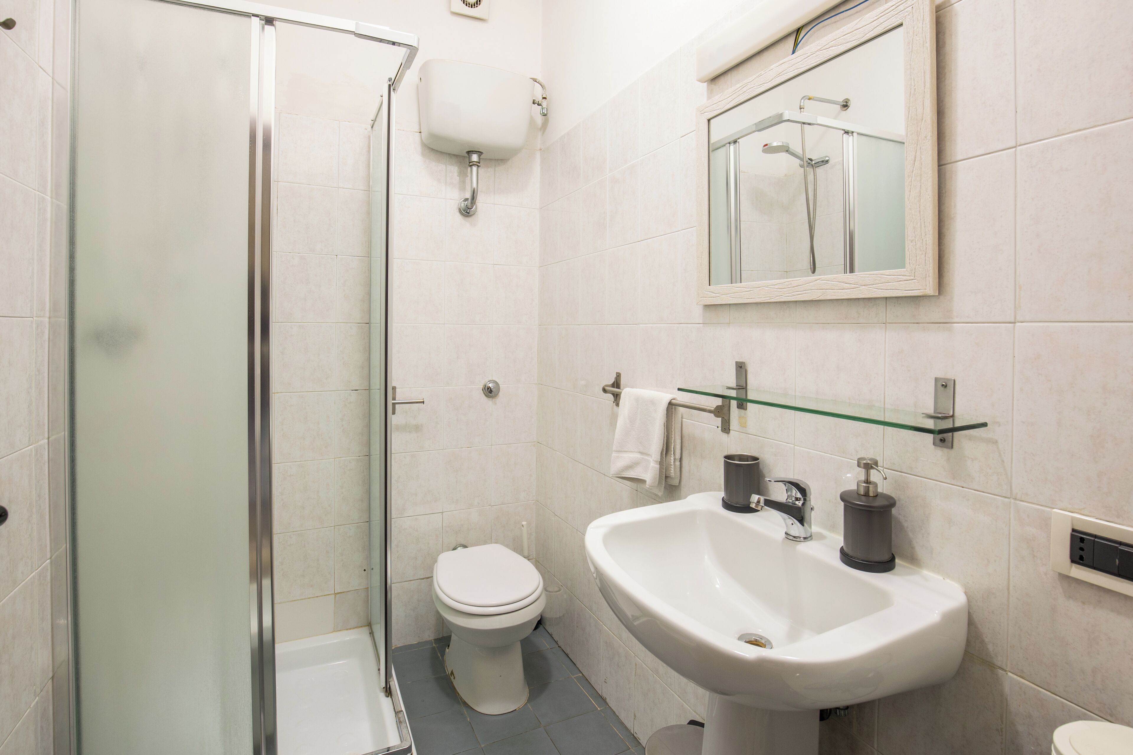 Un baño con cabina de ducha de vidrio, inodoro blanco y lavamanos con espejo.