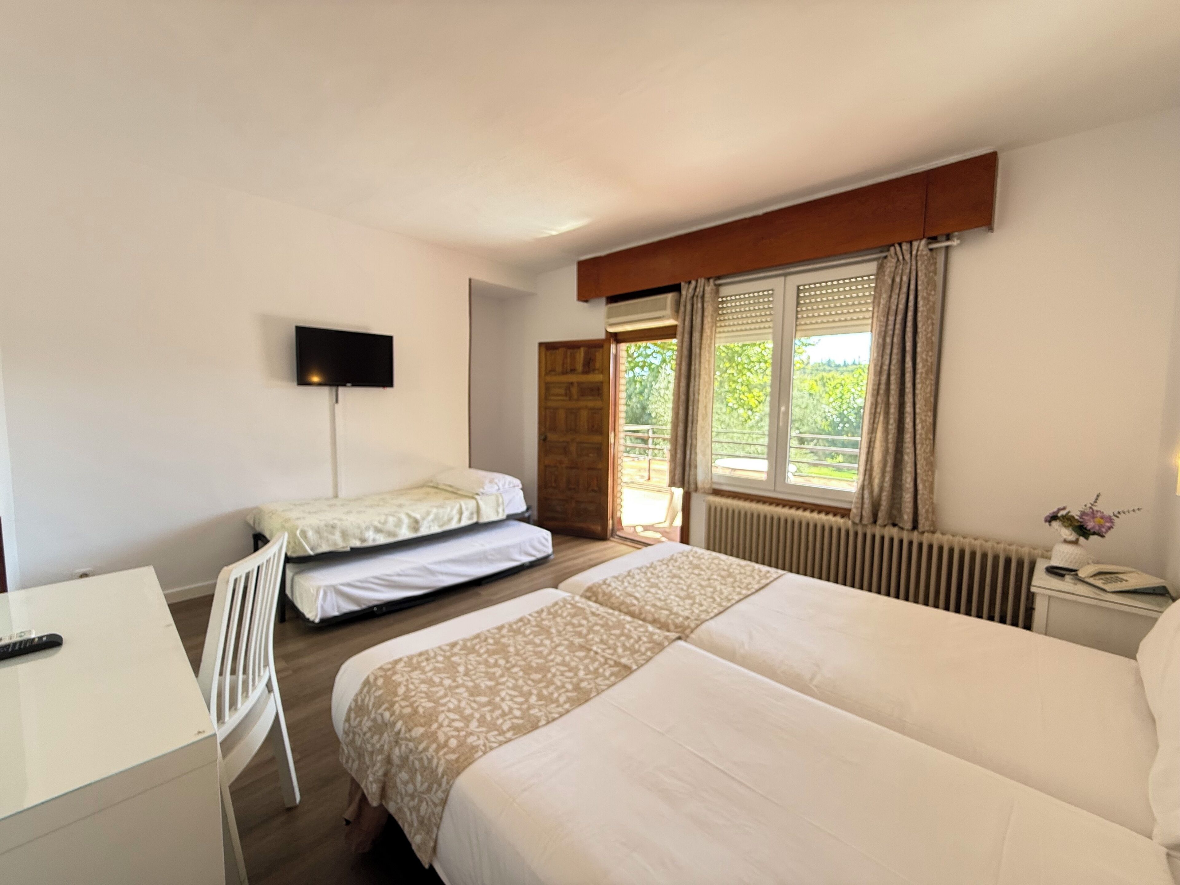 Un dormitorio con dos camas, un escritorio, un televisor y una ventana con cortinas.