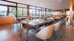 A spacious dining area with multiple tables and chairs, large windows offering views of the outdoors, and a television mounted on the wall. - Hotel Los Olivos (Getafe)