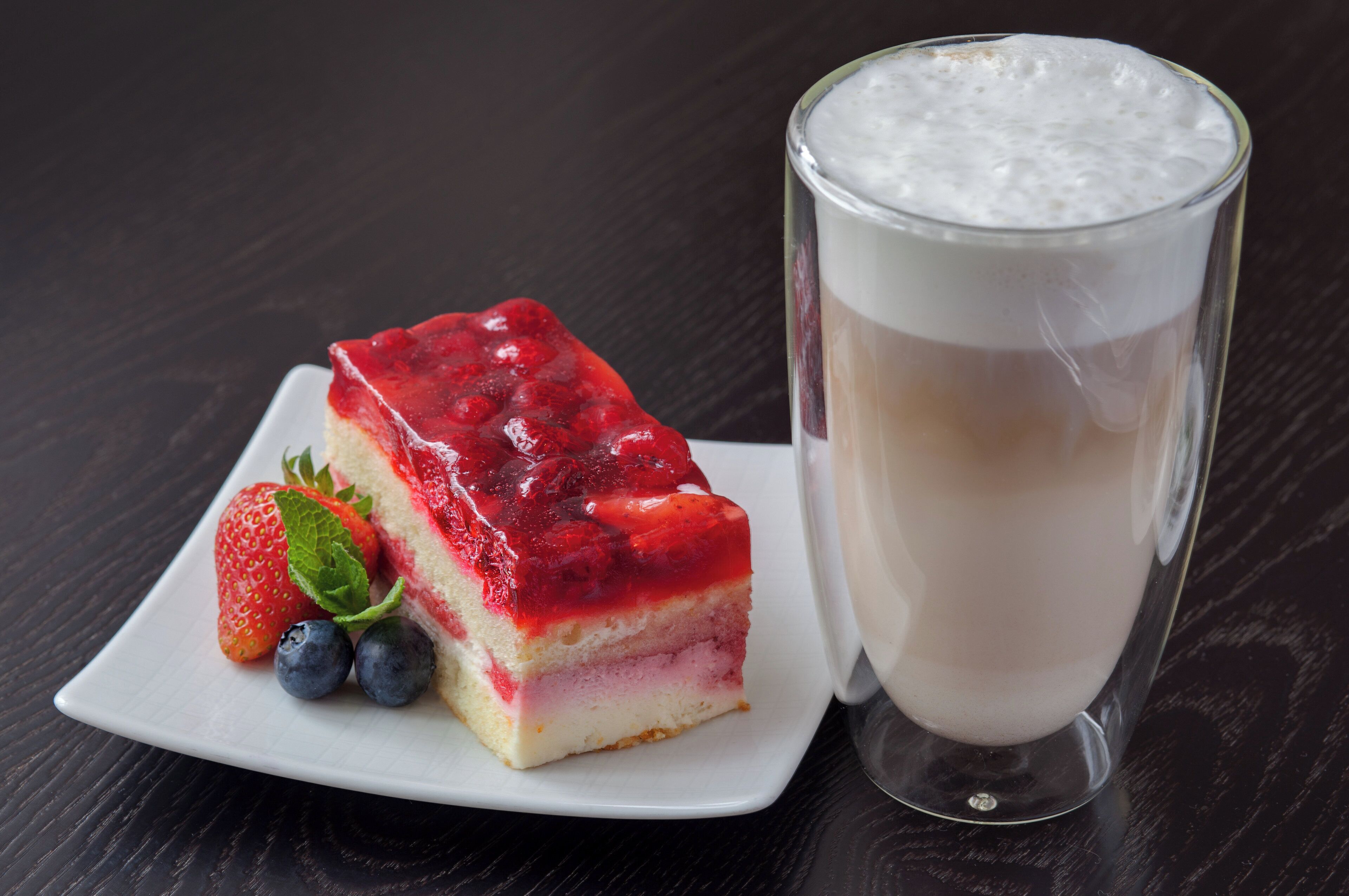 A slice of layered dessert with a red topping and a glass of milk.